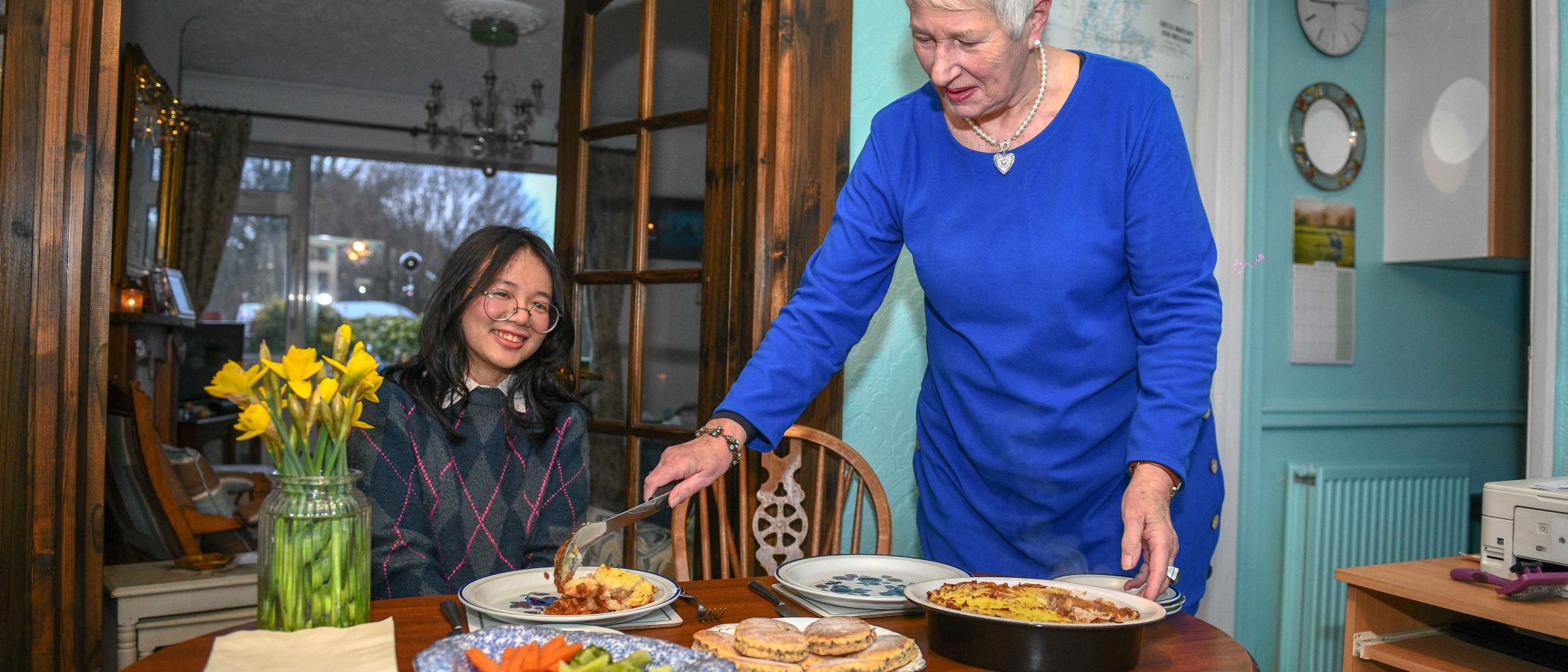 An international student sitting at a dining table while their host serves them food