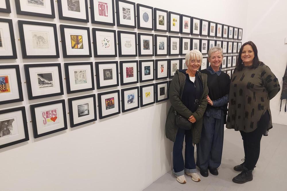Three people standing in front of a wall of framed prints