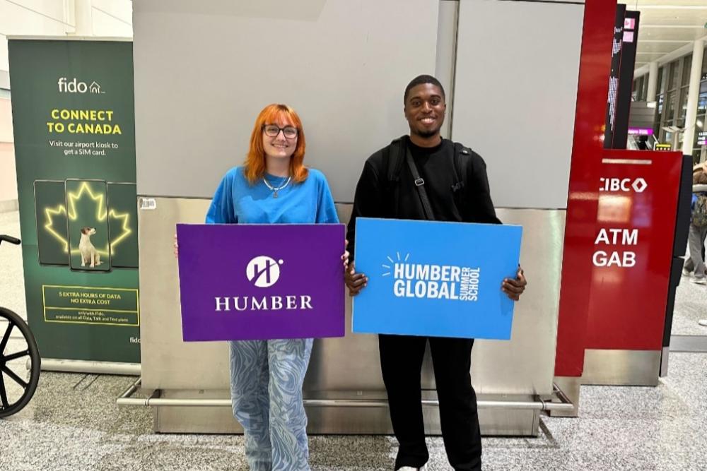 Two people holding Humber Global Summer School banners