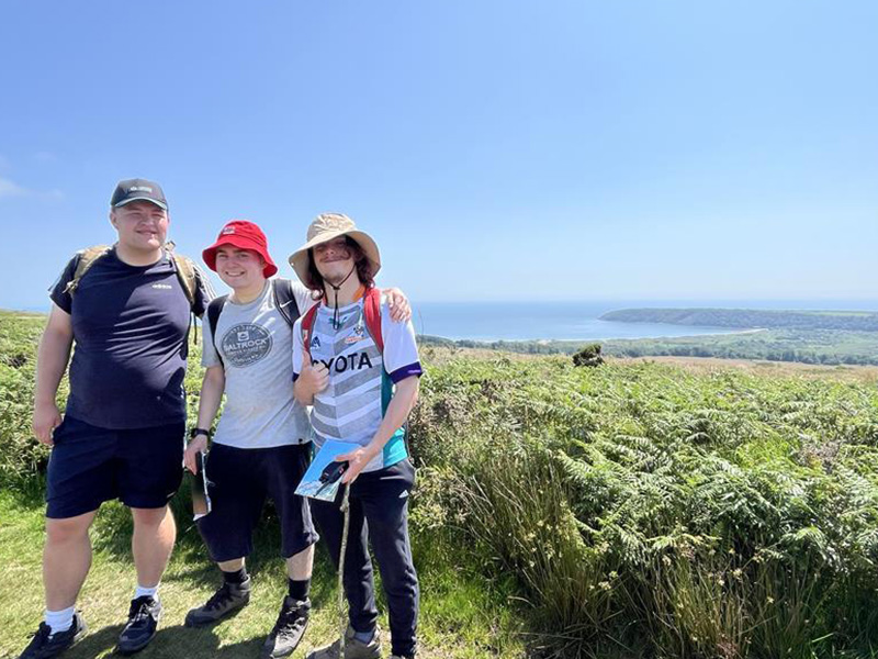 Three ILS students in Gower, with a view of the sea in the background