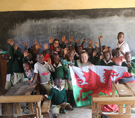 School children holding Welsh flag. The blackboard behind has numbers written in English, Swahili and Welsh