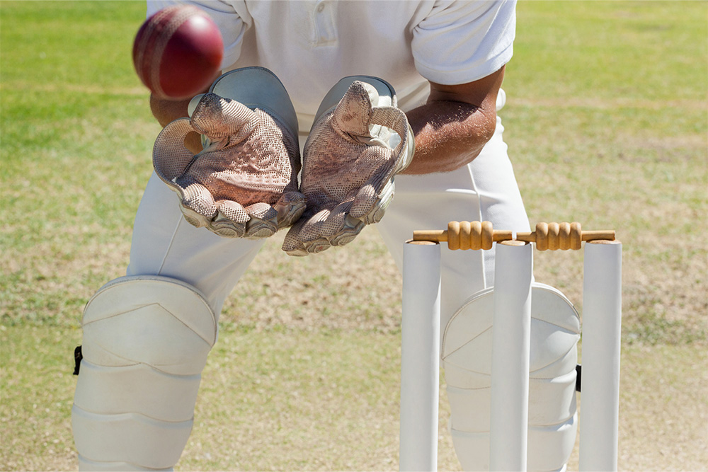 Close up of cricket wicket with someone catching the cricket ball