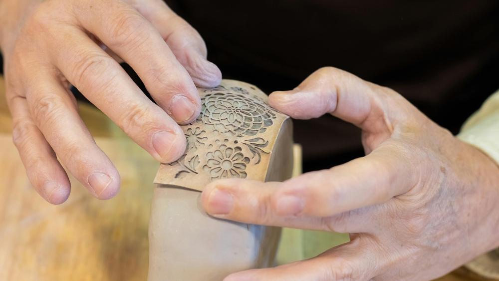 Person using stencil to make shapes on clay pot