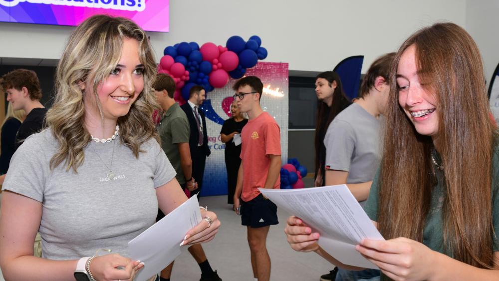 Two students holding paper and smiling