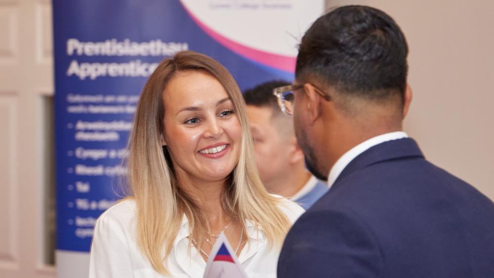 Two people chatting with a Gower College Swansea apprenticeship banner behind them