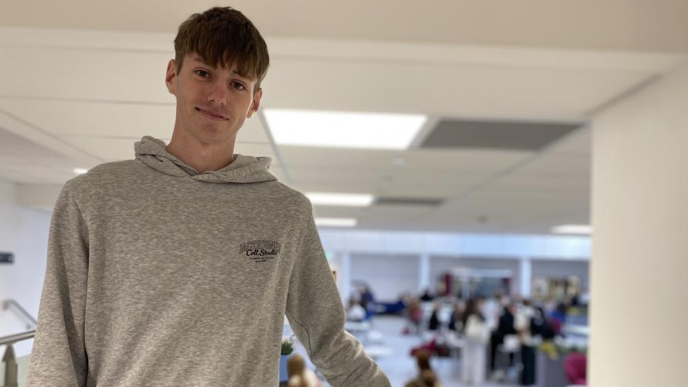 Student in grey hoodie standing in college area
