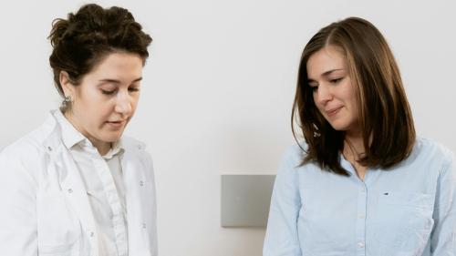 A clinical healthcare professional sits with a patient.