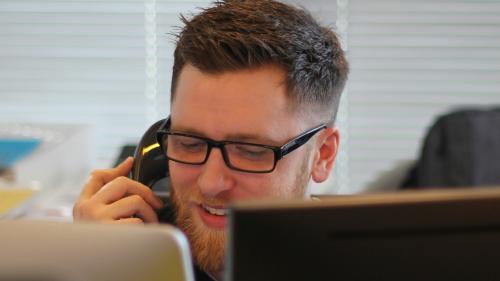 A person working in a contact-centre smiles whilst on call with a customer. 