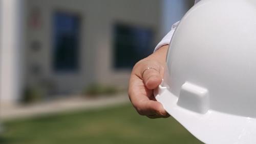 A person wearing high visibility clothing holds a hard hat.