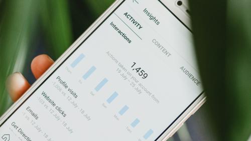 A person holds a phone, which displays various social media insights and statistics. 