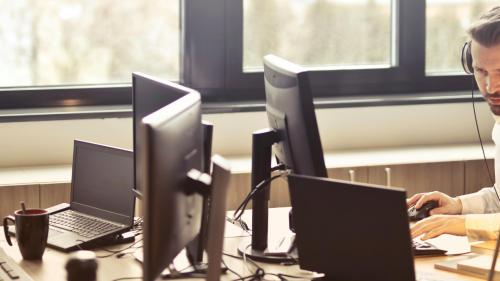 A person wearing headphones works at their desk in an IT helpdesk environment. 