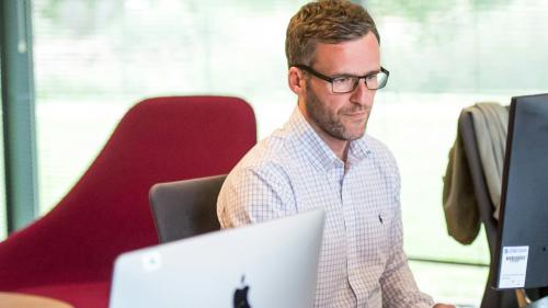 Grŵp o bobl yn gweithio ar eu cyfrifiaduron mewn swyddfa. 