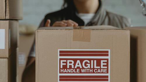 Boxes on shelf labelled as fragile, with a person going to pick one up