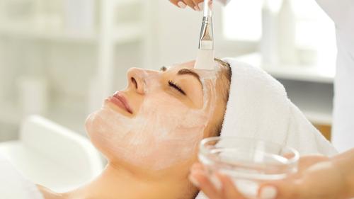 Beauty therapist applies skin peeling treatment to client with brush
