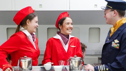 Two travel students in cabin crew uniform and one student in a pilot uniform practicing in the mock-up of a plane