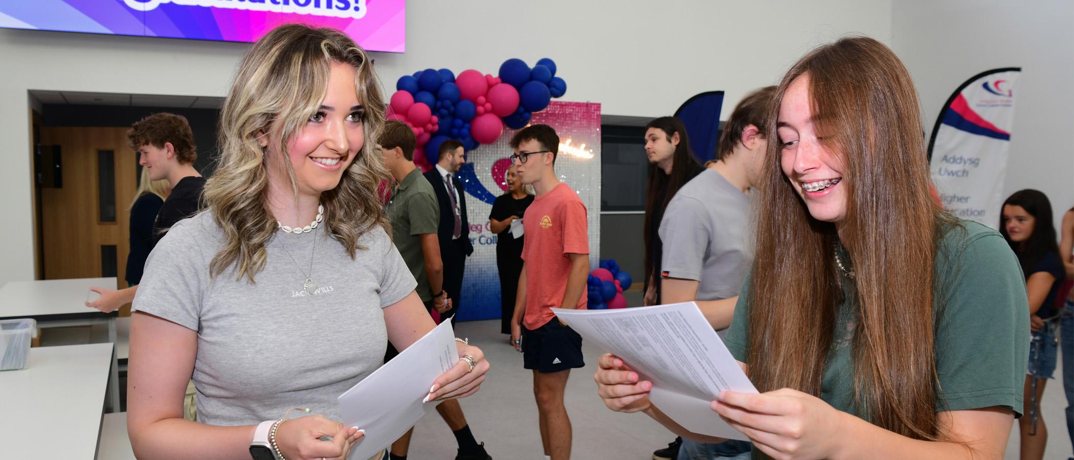 Two students holding paper and smiling