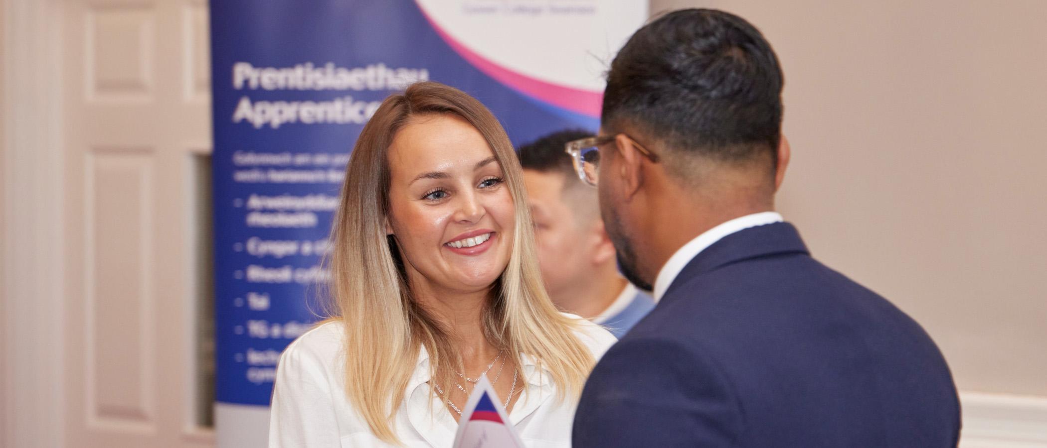 Two people chatting with a Gower College Swansea apprenticeship banner behind them