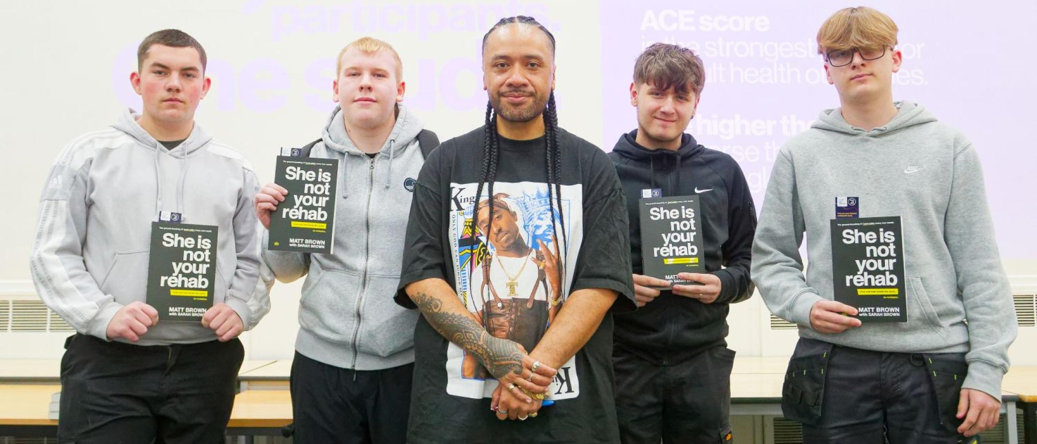 Man in black t-shirt, standing with male students holding books