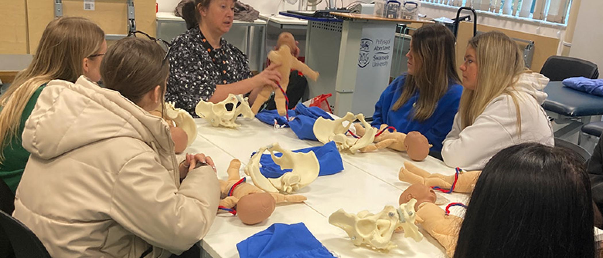 Learners sitting at table learning midwifery with dolls