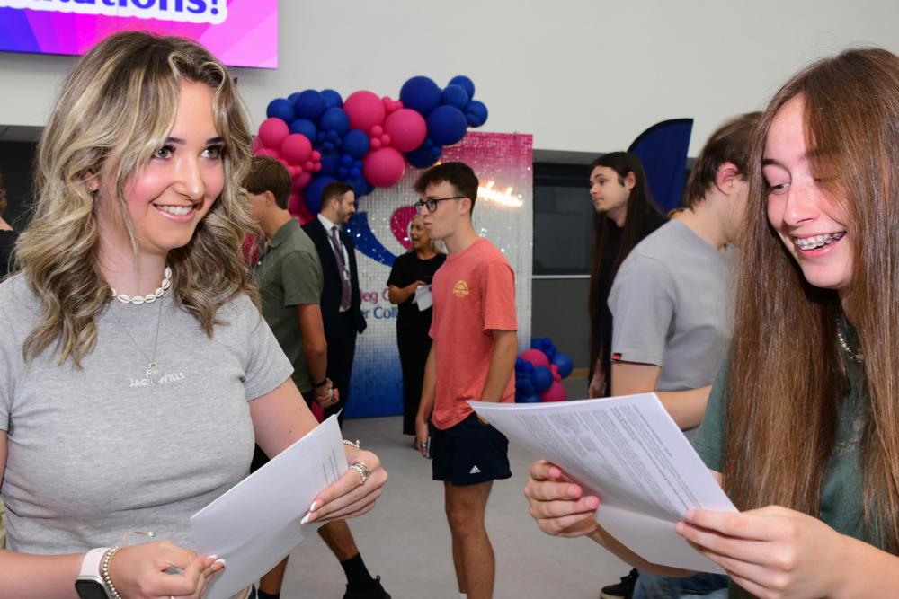 Two students holding paper and smiling