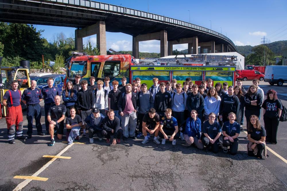 Large group of people standing next to fire engine, bridge in background and blue sky