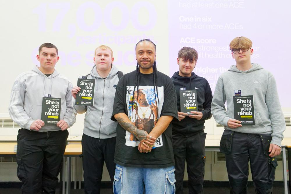 Man in black t-shirt, standing with male students holding books