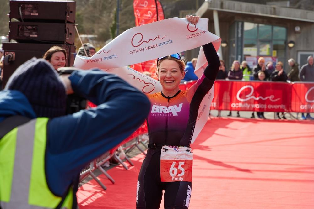 Female winner of Mumbles Duathlon holding a banner at the finish line