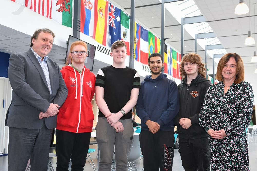 Llun grŵp o staff a myfyrwyr gyda baneri yn y cefndir / Staff and students group photo with flags in background 