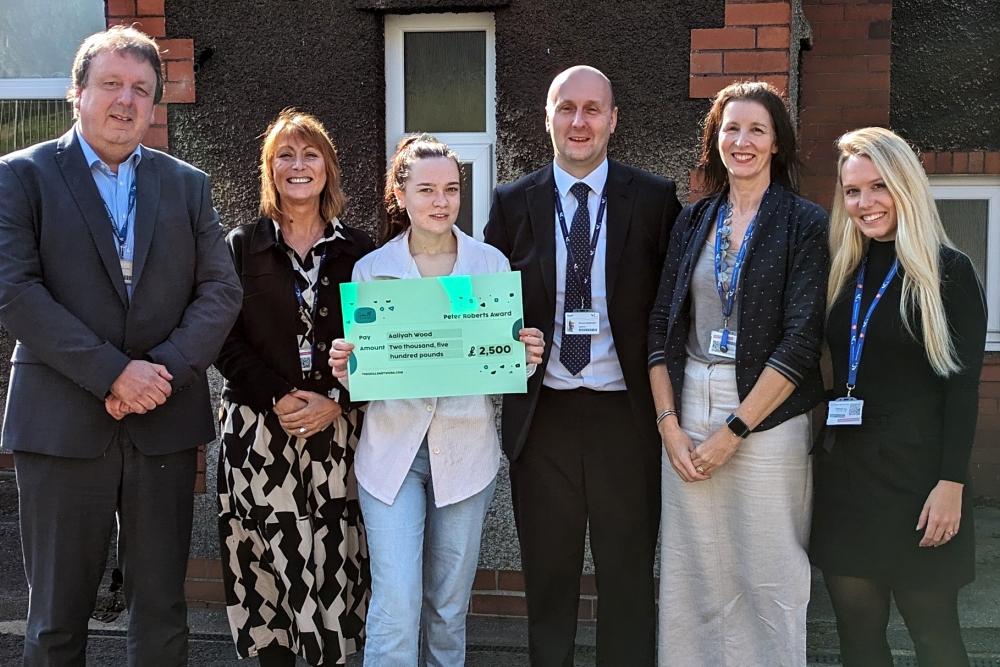 Group of people outside building, one holding cheque