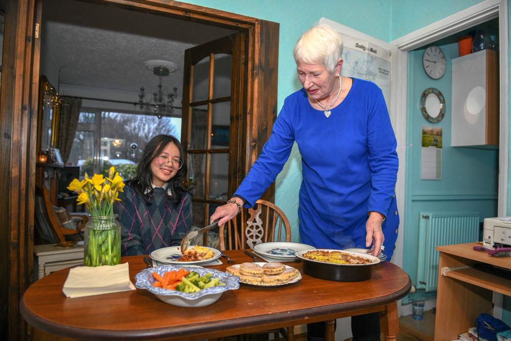 An international student sitting at a dining table while their host serves them food