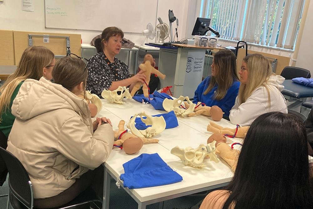 Learners sitting at table learning midwifery with dolls